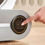 Hand pressing control panel on automatic self-cleaning cat litter box with touchscreen display showing Clean, Auto, and Remove odor functions
